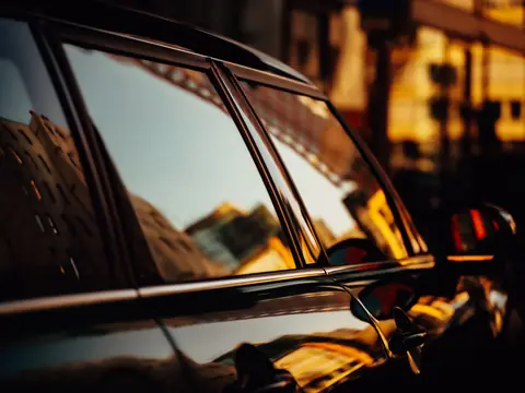 The side windows of a dark car reflecting buildings at sunset