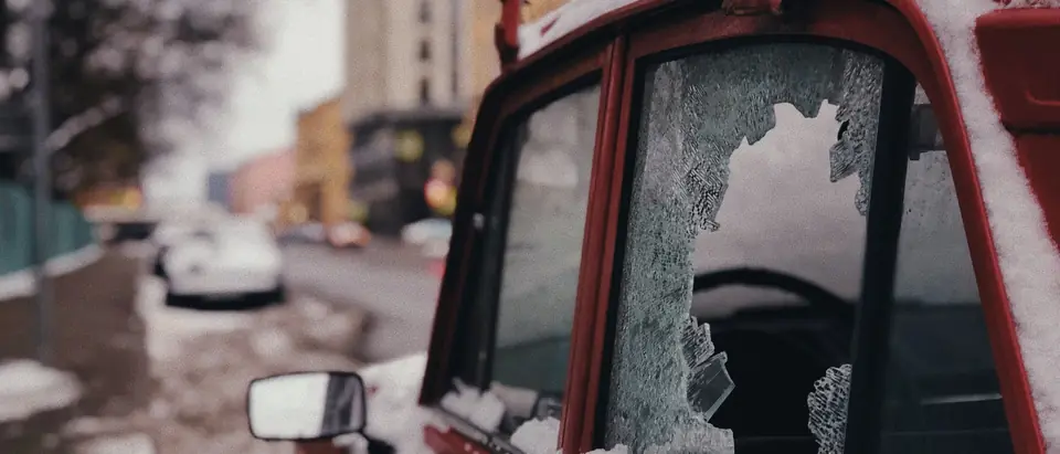 A door window broken out of a parked car in snow