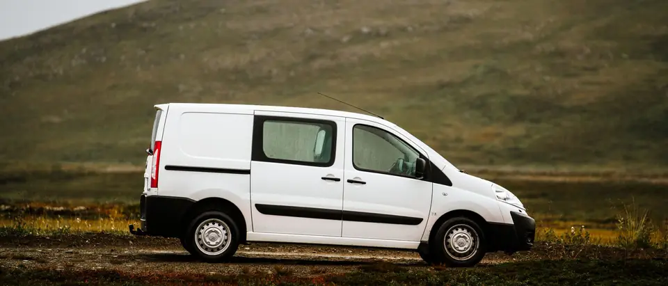 A plain white van parked at the edge of a field at dusk