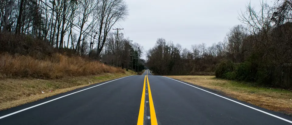 An empty two-lane road with a double yellow line between bare trees