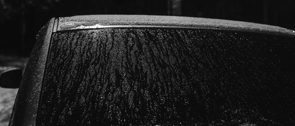 The frosted rear window of a dark car, in black and white