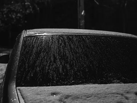 The frosted rear window of a dark car, in black and white