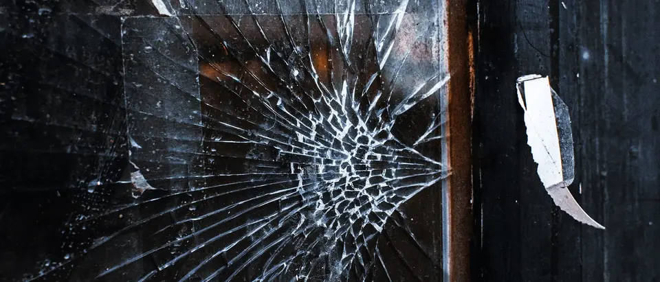 Cracks running out from one impact point in a dark pane of glass