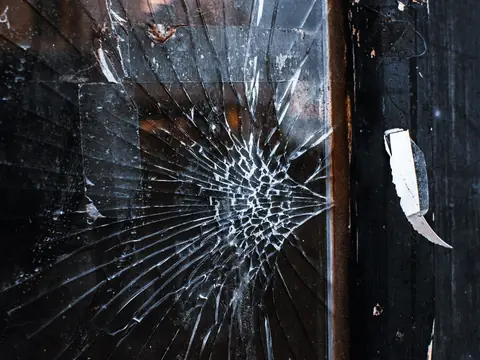 Cracks running out from one impact point in a dark pane of glass