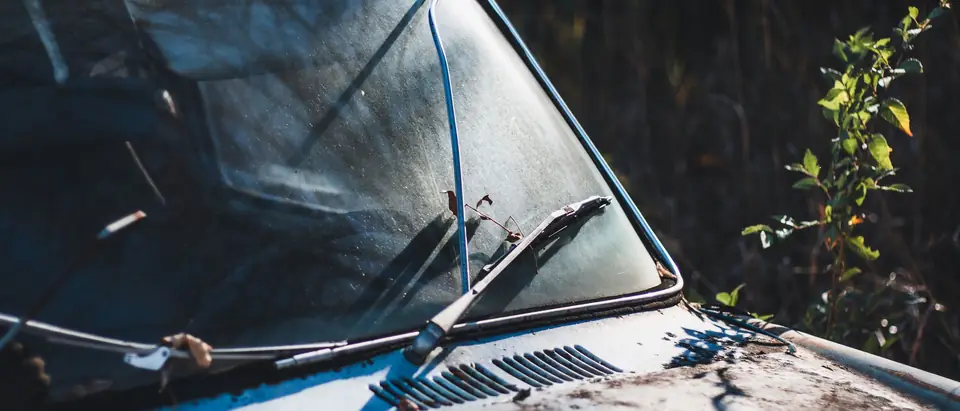 An old windshield and its wiper on a weathered car, close up